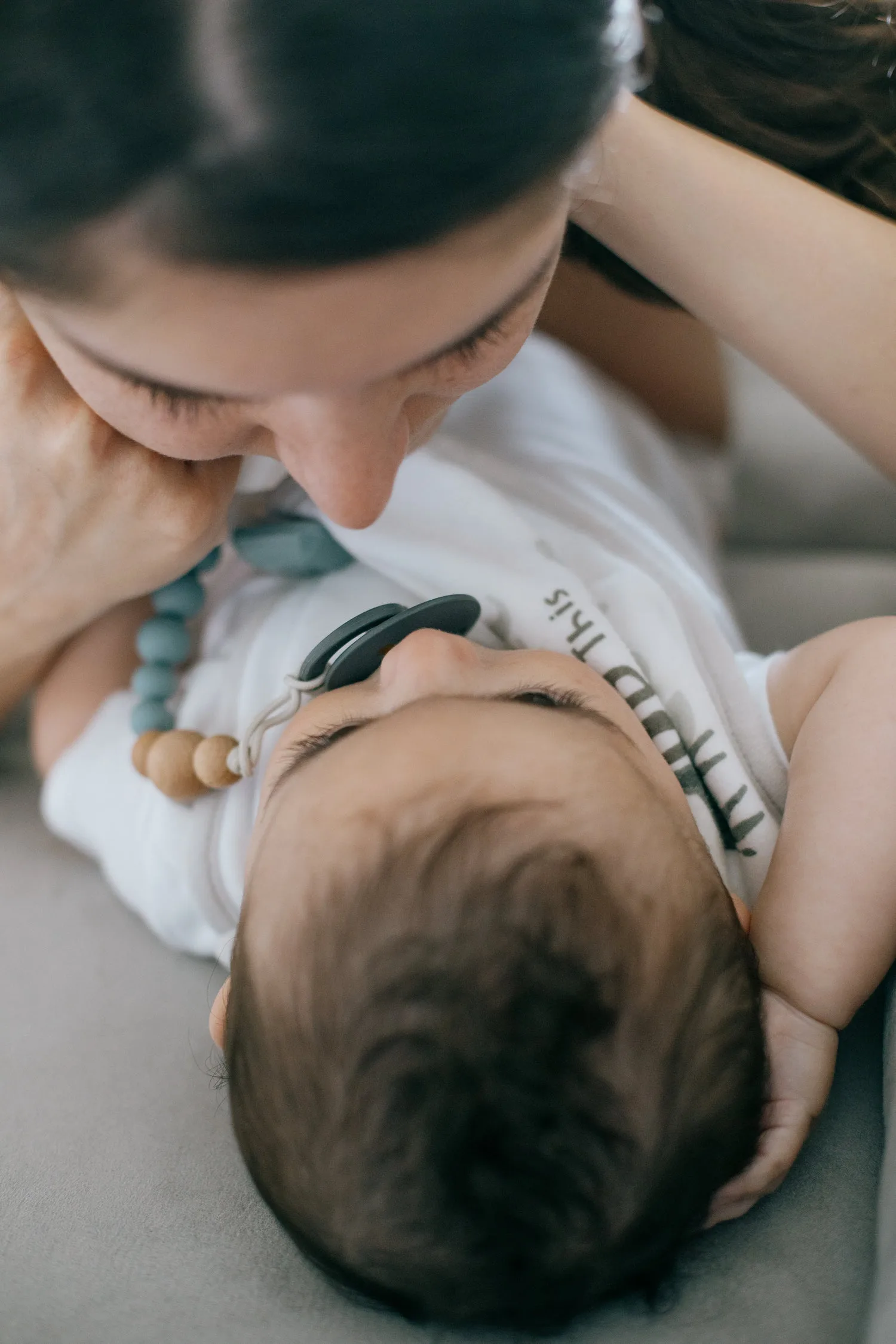 Jeune maman réconfortant son bébé avec une tétine et un collier de portage coloré