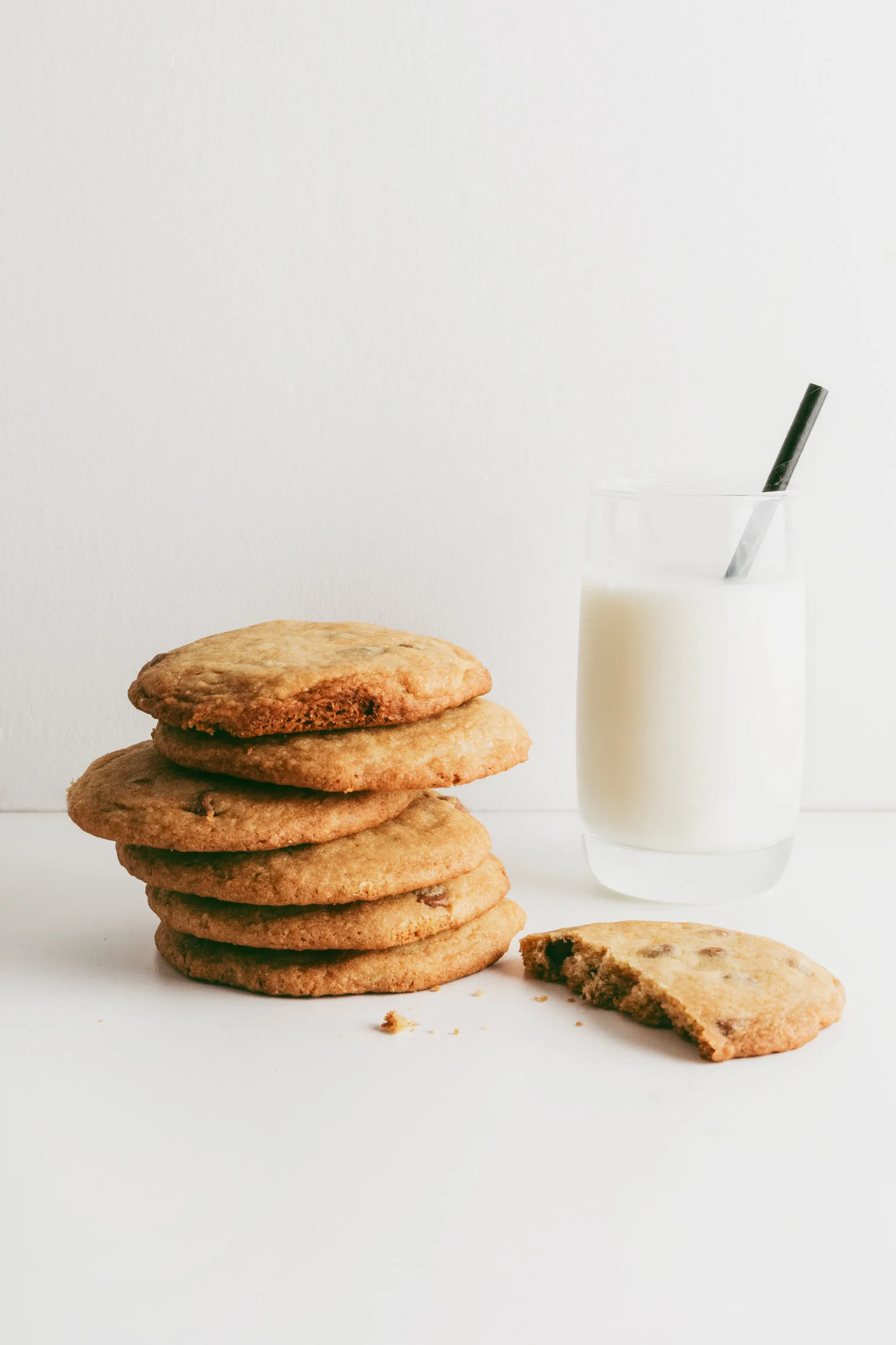 Pile de cookies moelleux au chocolat posés à côté d un verre de lait sur un fond blanc