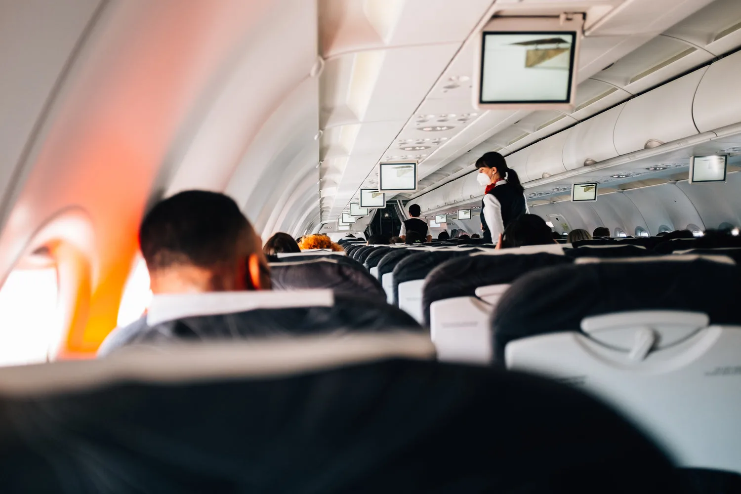Vue de l intérieur d un avion commercial avec rangées de sièges et hôtesse de l air