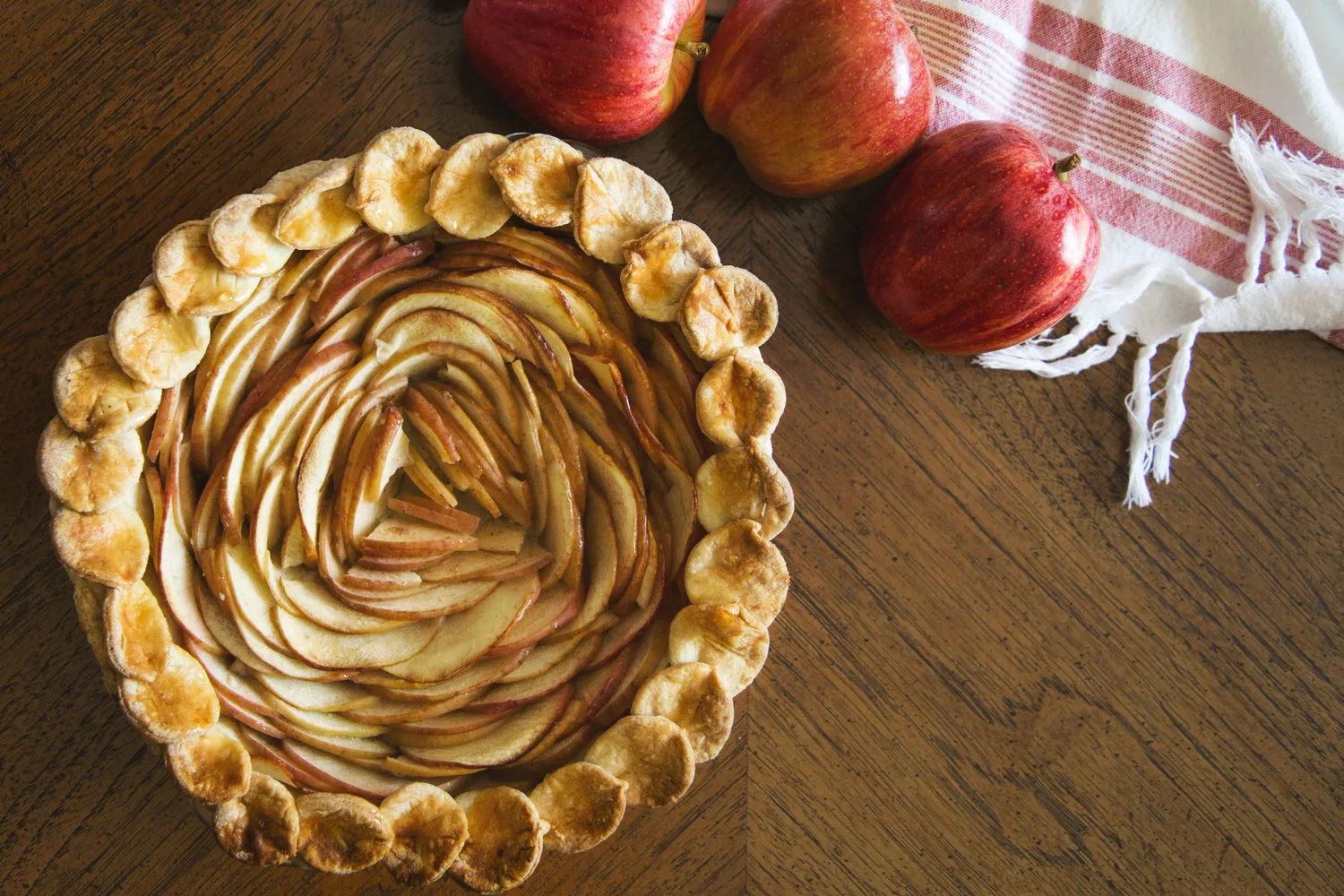 Tarte aux pommes dorée présentée sur une table en bois avec pommes fraîches et torchon rayé