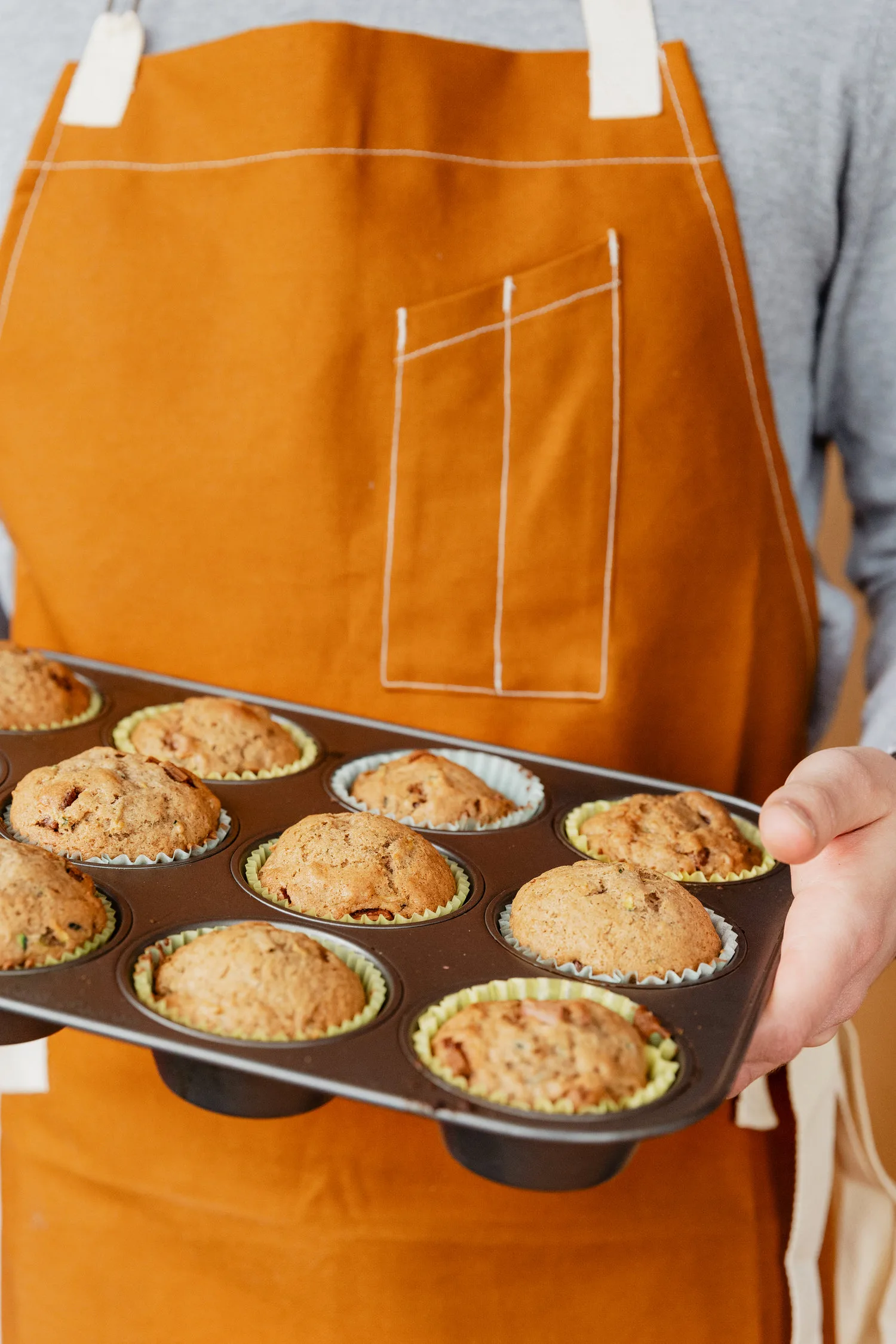 Boulanger tenant une plaque de muffins dorés fraîchement sortis du four dans un tablier