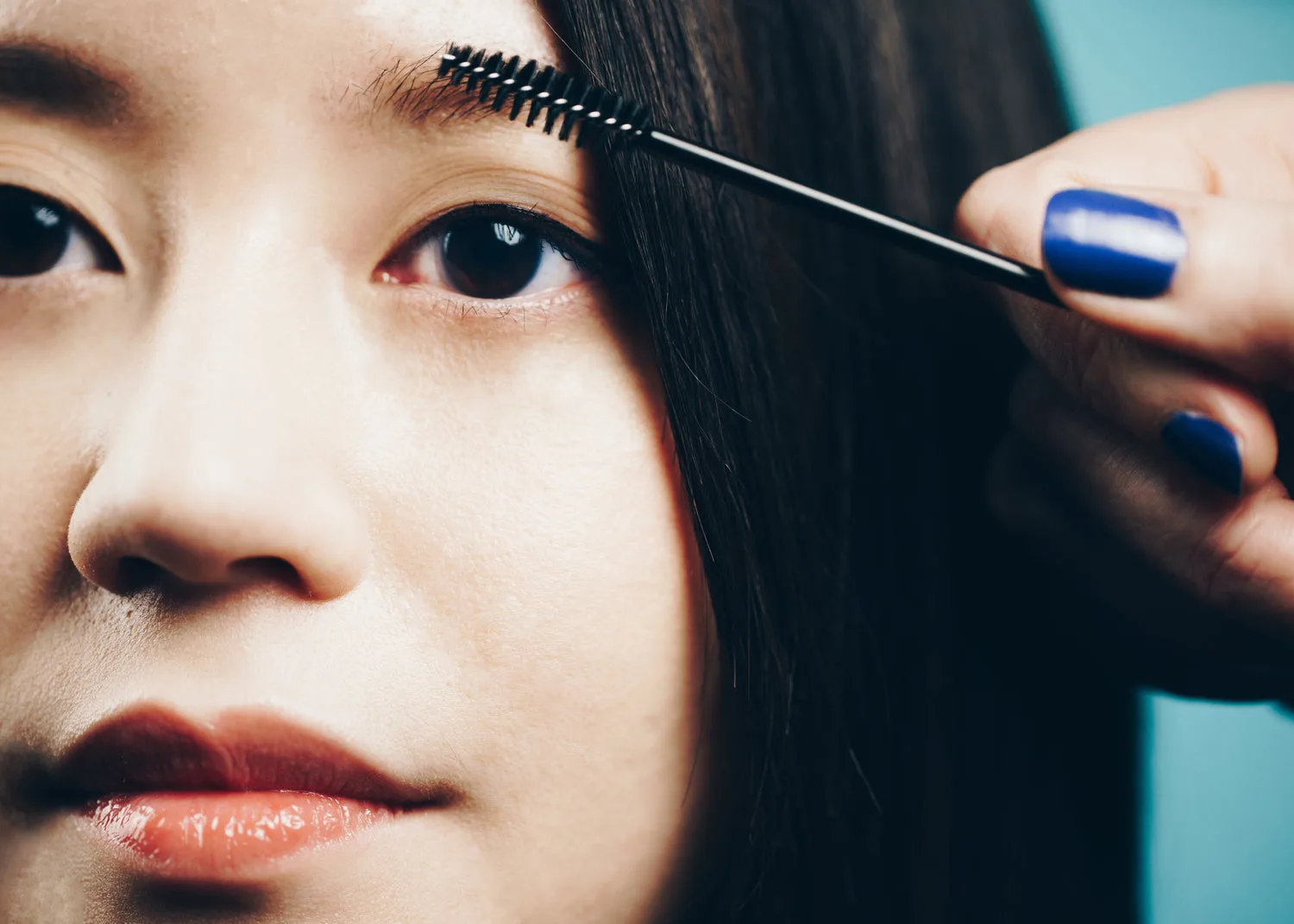 Femme se brossant les sourcils avec un goupillon en gros plan sur fond bleu