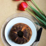 Gâteau au yaourt bundt cake doré dans une assiette blanche avec tulipes rouges à côté
