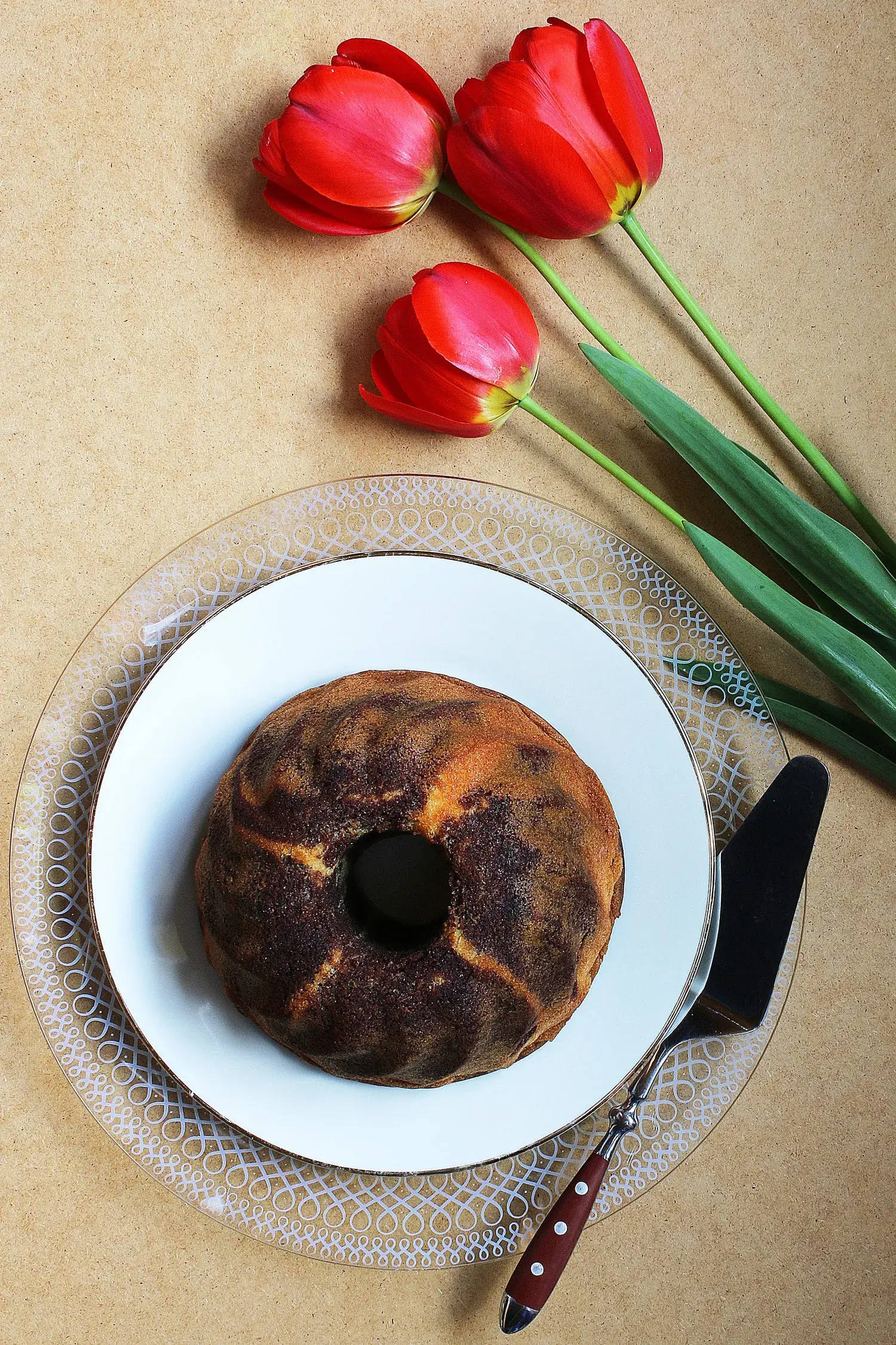 Gâteau au yaourt bundt cake doré dans une assiette blanche avec tulipes rouges à côté