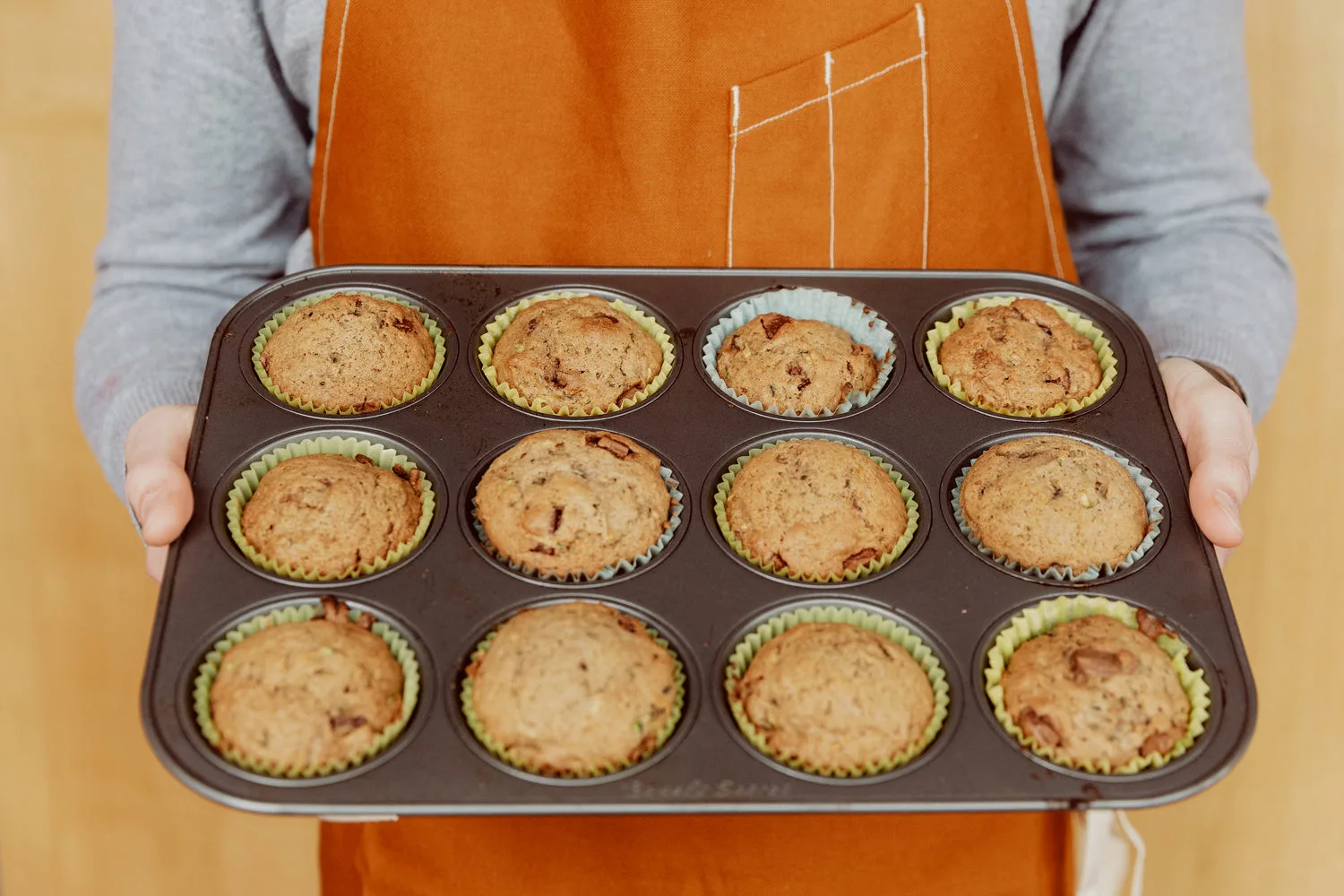 Plaque de 12 muffins au chocolat dorés tenue par un cuisinier en tablier orange
