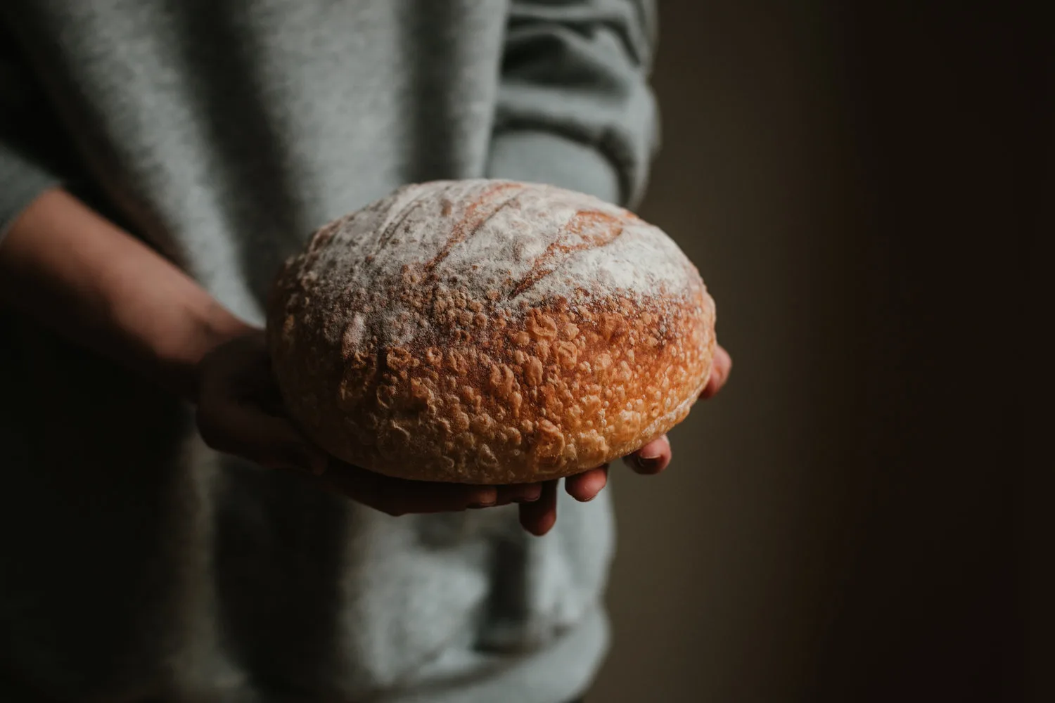 Mains tenant une belle miche de pain de campagne maison farinée avec croûte dorée