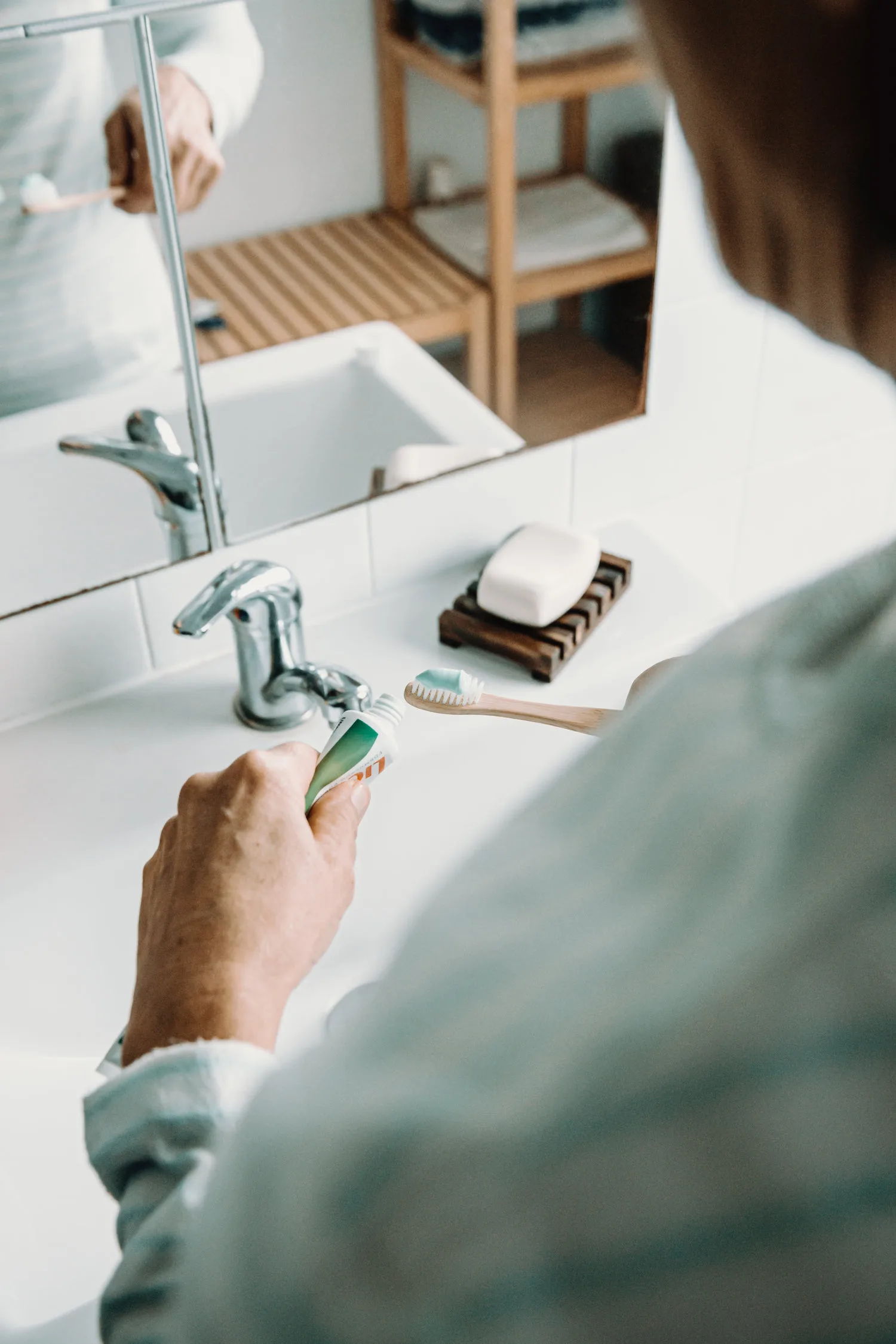 Mains appliquant du dentifrice sur une brosse à dents en bambou au-dessus d un lavabo