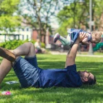 Père allongé dans l herbe soulevant son bébé en souriant pendant les vacances en famille
