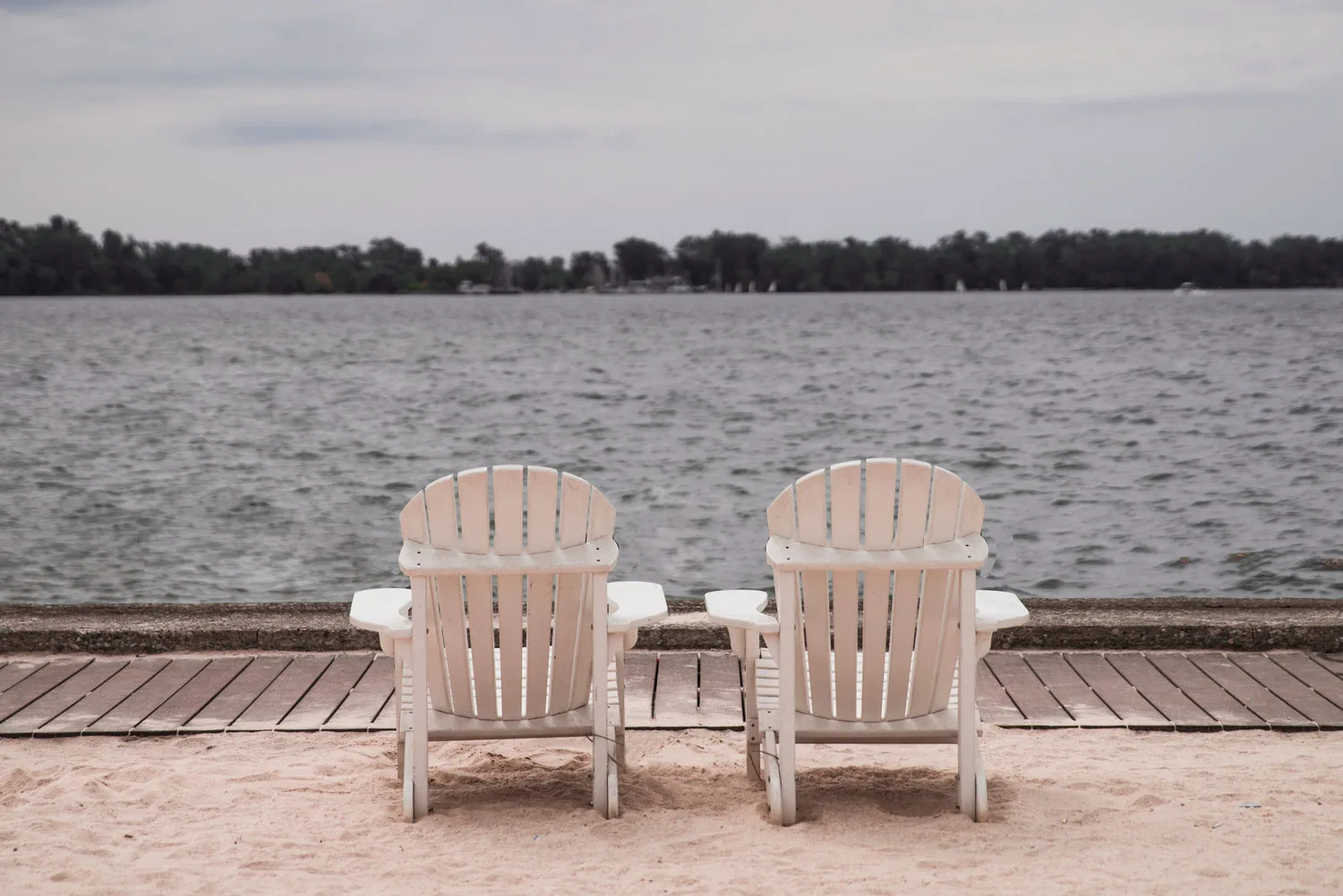 Deux chaises longues en bois posées sur ponton de sable face à un lac paisible