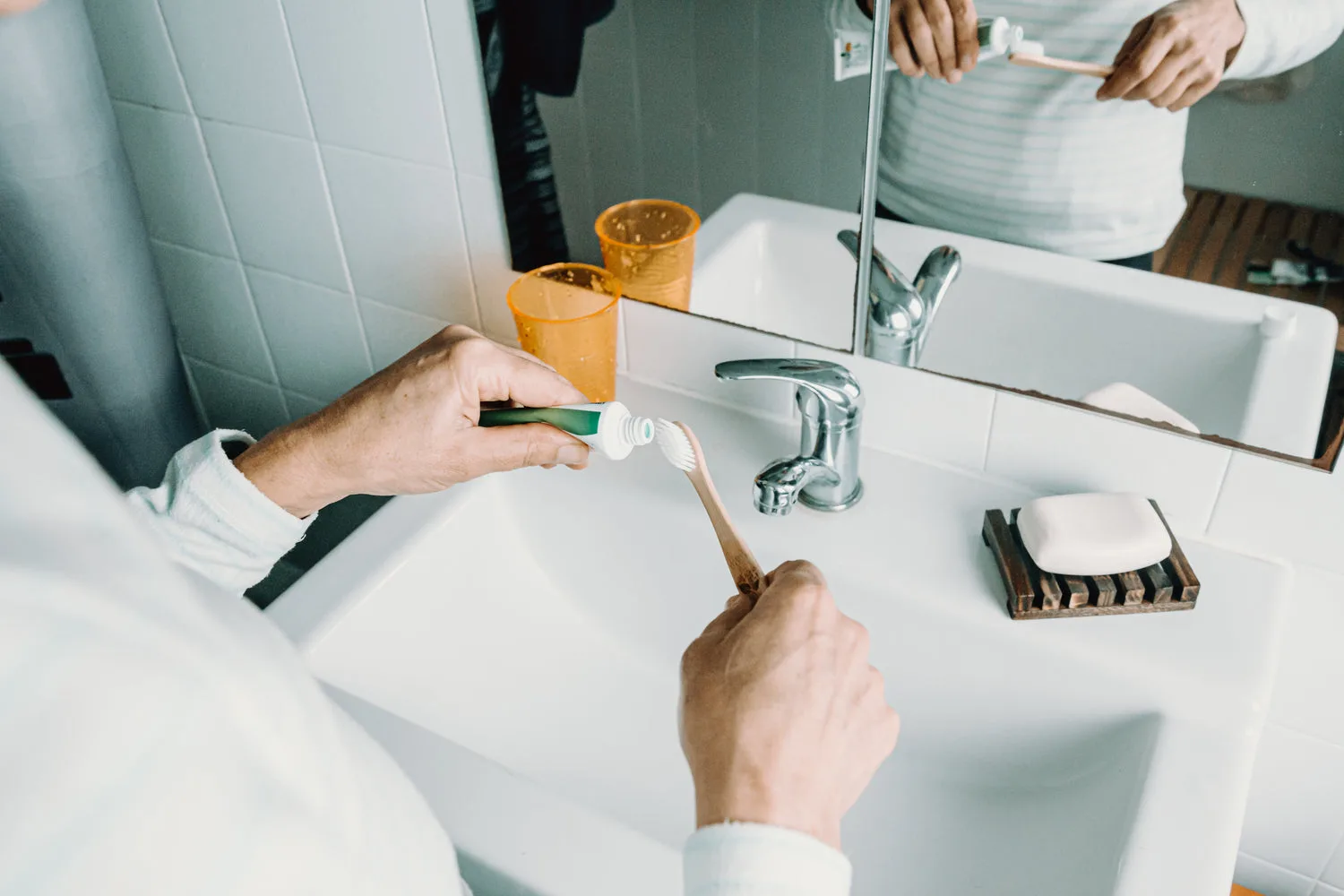 Personne tenant une brosse à dents en bambou et un tube de dentifrice au-dessus d un lavabo blanc