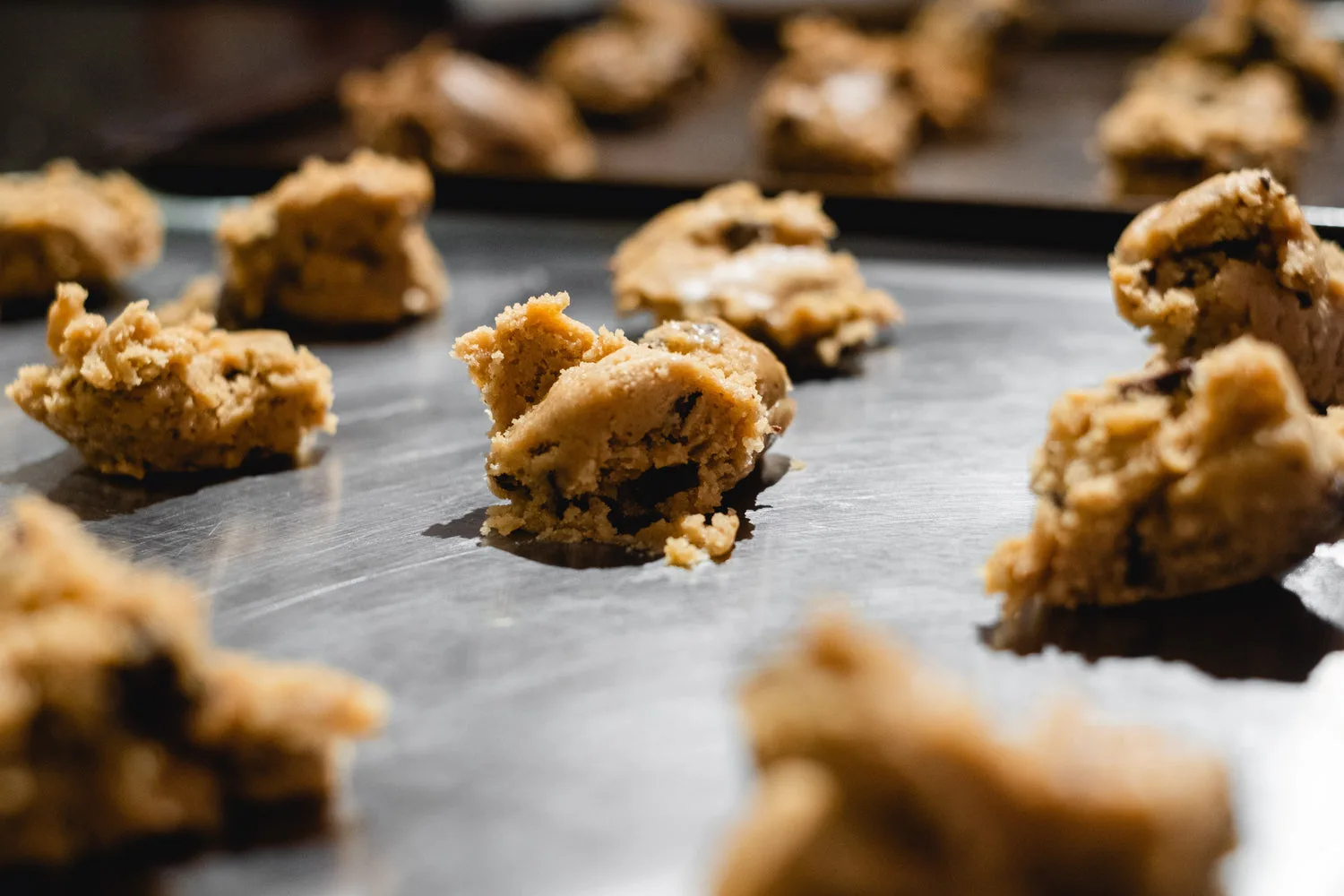 Boules de pâte à cookies crue posées sur une plaque de cuisson métallique prêtes à enfourner