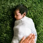 Nouveau-né endormi emmailloté dans un lange blanc sur fond vert naturel