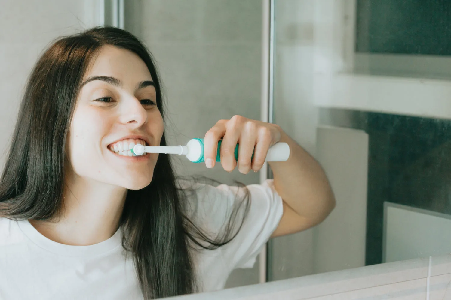 Jeune femme se brossant les dents avec une brosse à dents électrique devant un miroir