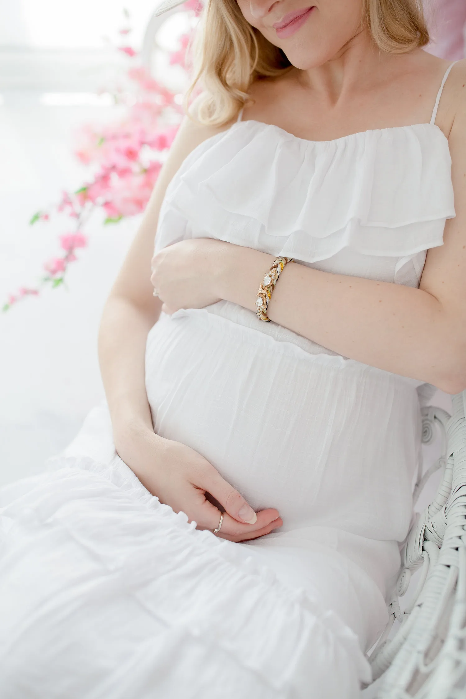 Jeune femme enceinte en robe blanche assise tenant délicatement son ventre dans une pièce lumineuse