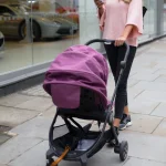 Jeune maman poussant une poussette violette dans une rue commerçante urbaine