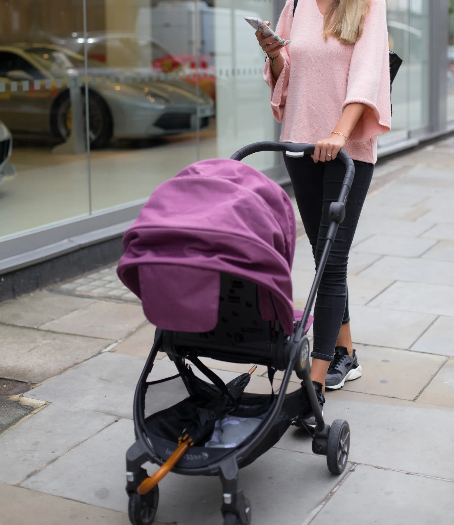 Jeune maman poussant une poussette violette dans une rue commerçante urbaine